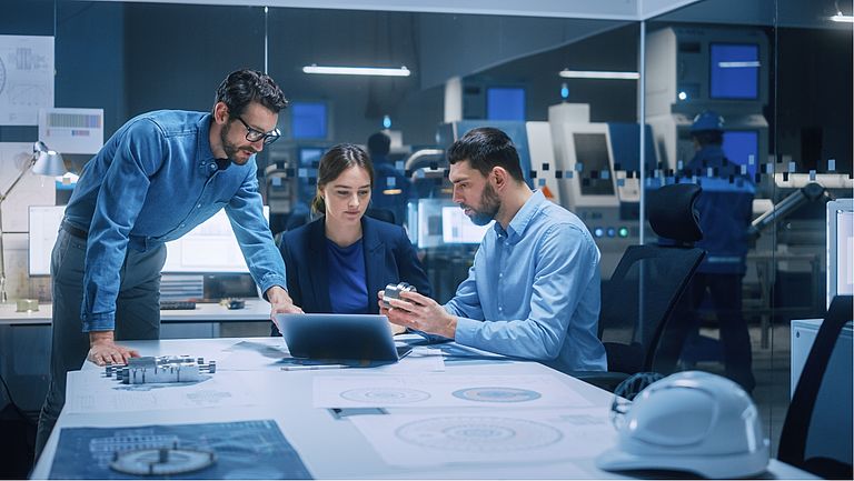 Ingenieurteam bespricht technische Zeichnungen und Produktionsdaten von Getrieben in moderner Entwicklungsumgebung
